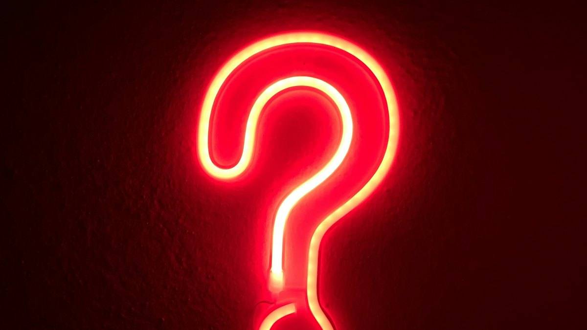 A red neon question mark on a dark wall
