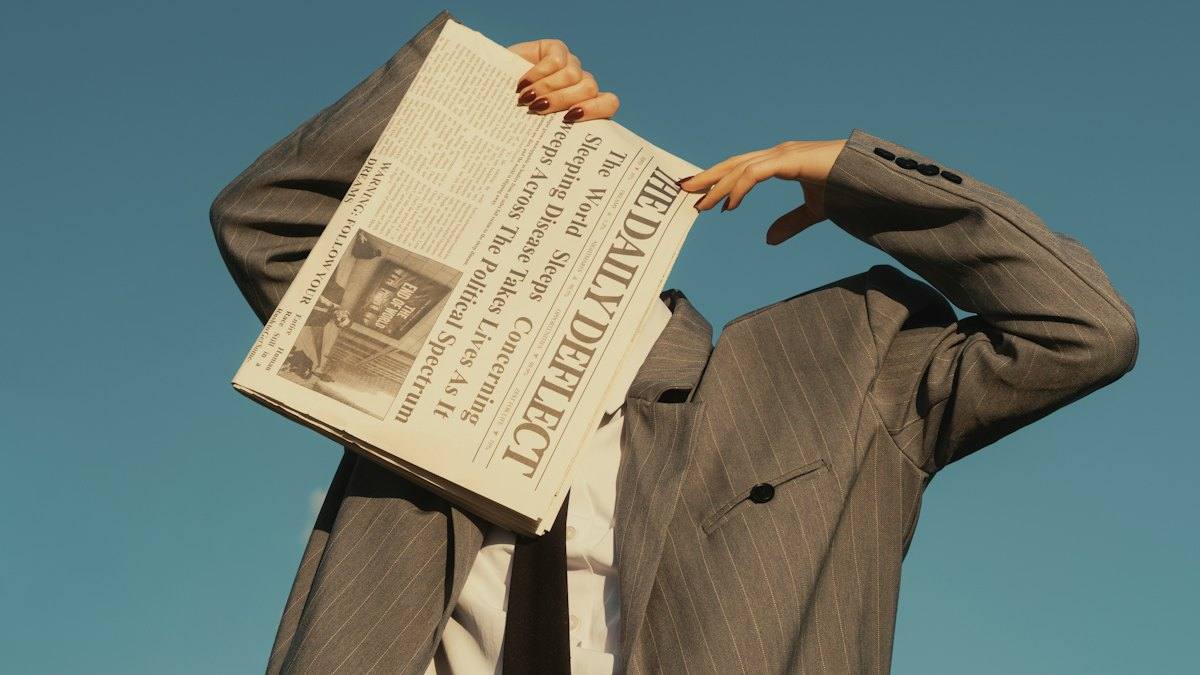 A person in a suit hiding their face behind a newspaper