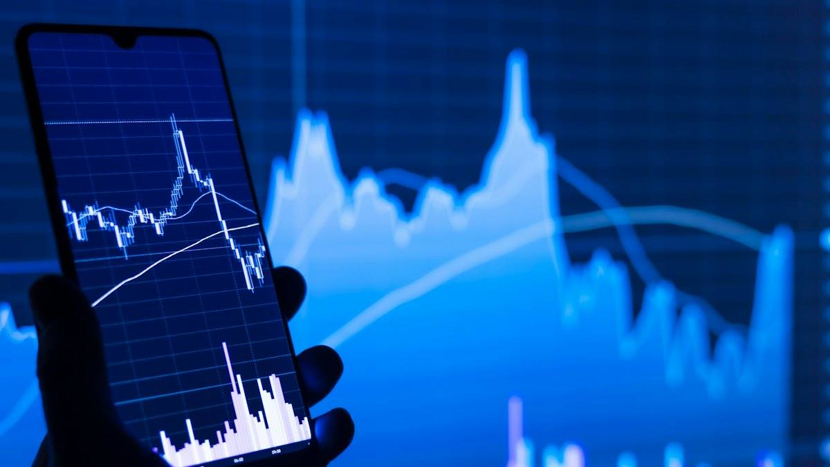 A phone showing a price chart in front of a larger chart